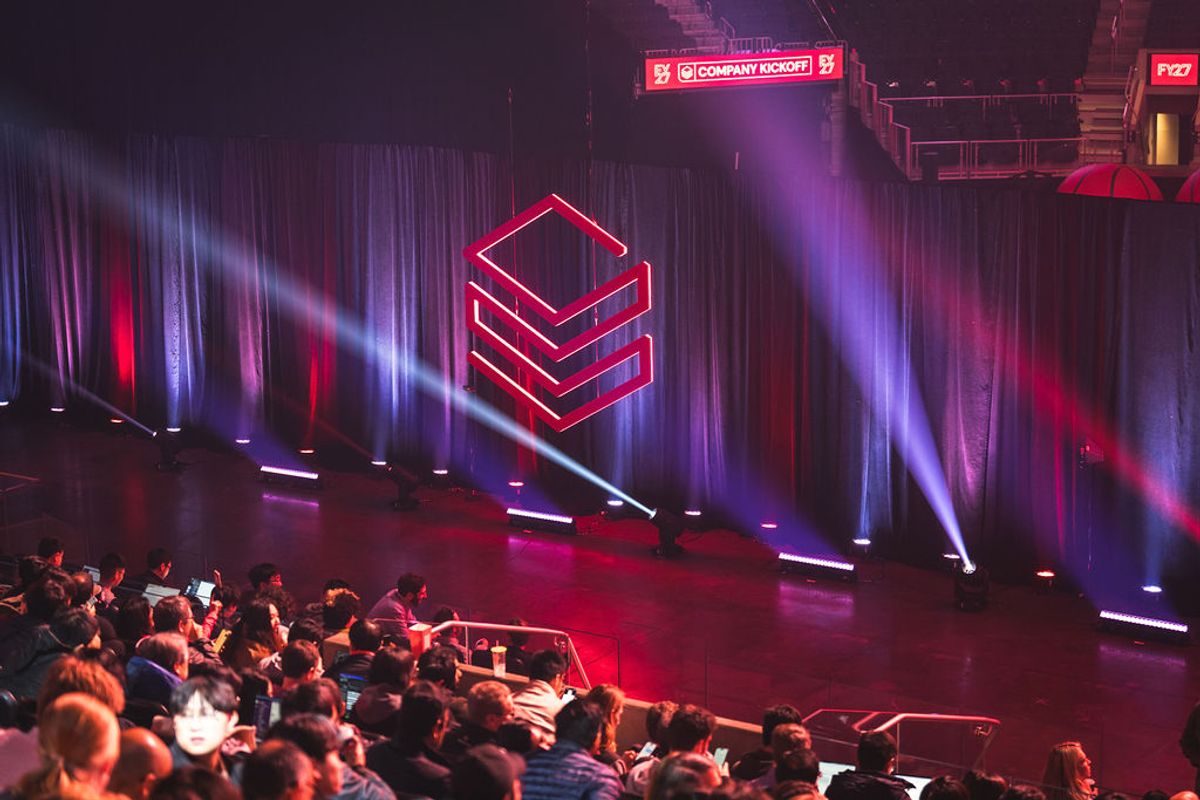 Conference attendees watching presentation on stage with geometric red logo and purple lighting