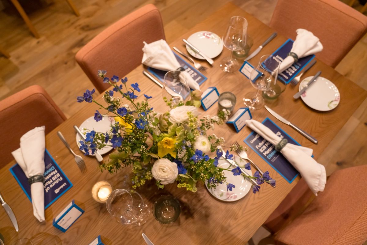 Elegant dinner table set for four with floral centerpiece, blue place cards, wine glasses, and salmon-colored.