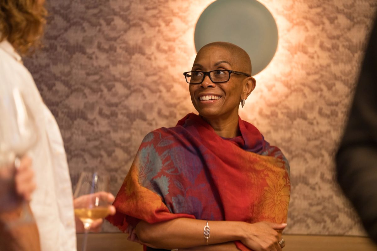 Smiling panelist in colorful wrap holds wine glass during discussion event at restaurant table
