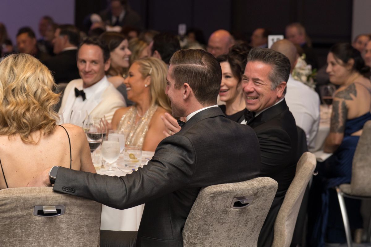 Formally dressed guests sitting at tables during an upscale evening event, with attendees socializing.