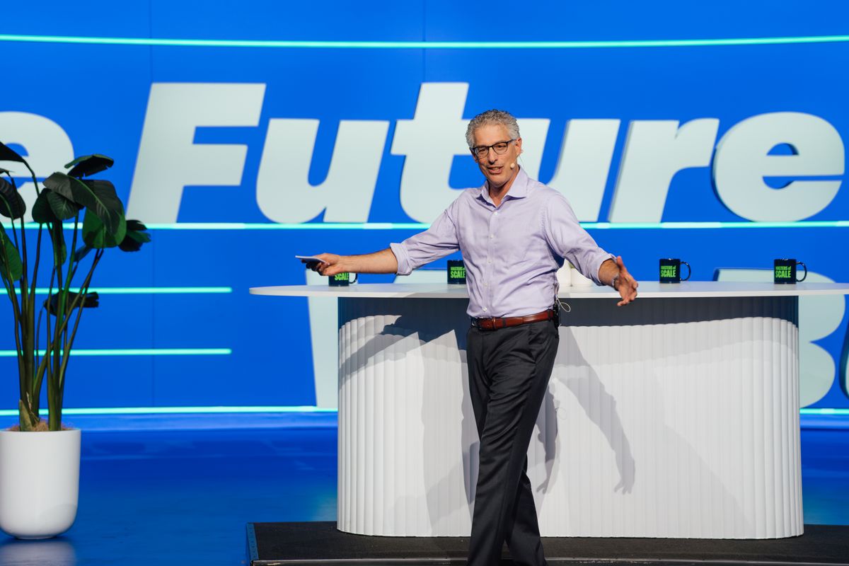 Executive presenting on stage at conference with blue backdrop and modern podium setup
