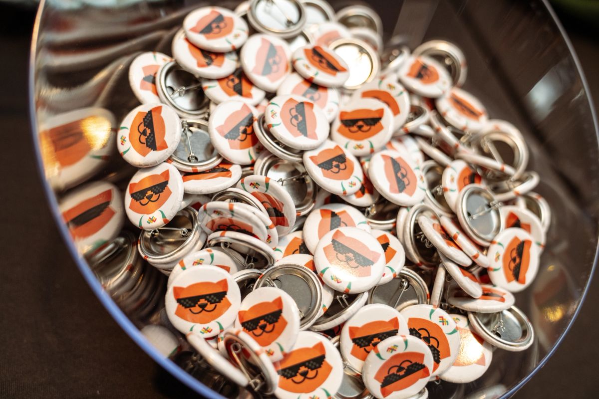 Bowl of white pin buttons featuring an orange cat mascot with sunglasses at a conference.