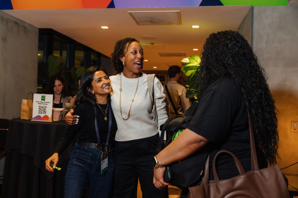 Three women networking and conversing at a conference event in a modern venue with colorful ceiling decor