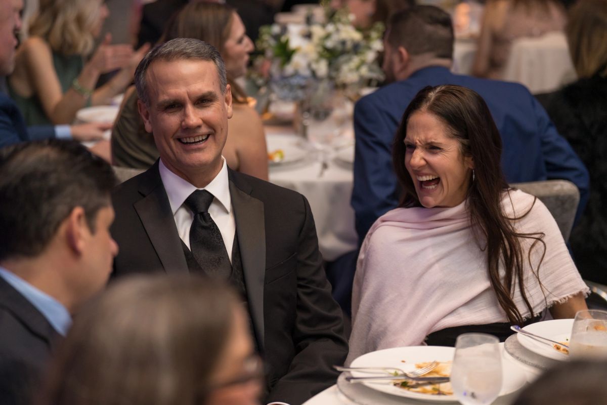 Two people laughing and enjoying conversation at a formal dinner event with elegantly set tables