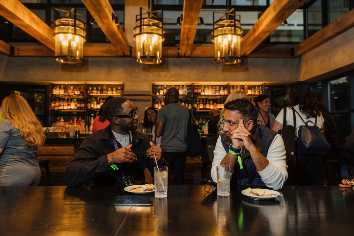 Two men in suits having drinks and conversation at an upscale restaurant bar with exposed beams and lanterns