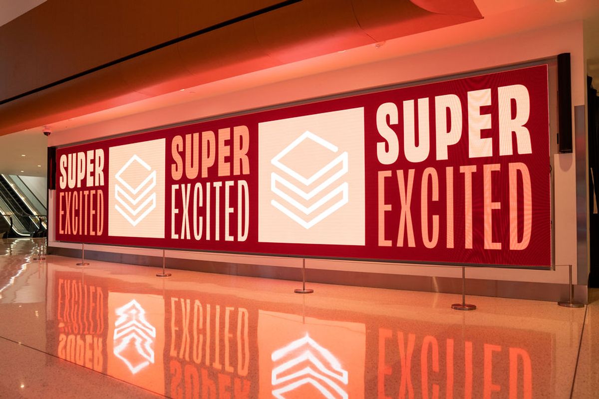 Large red banner displays "SUPER EXCITED" text with geometric logos in modern venue with polished floors