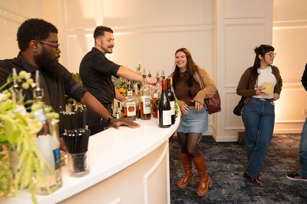 Bartender serves drinks to networking event attendees at white bar counter in elegant interior space.