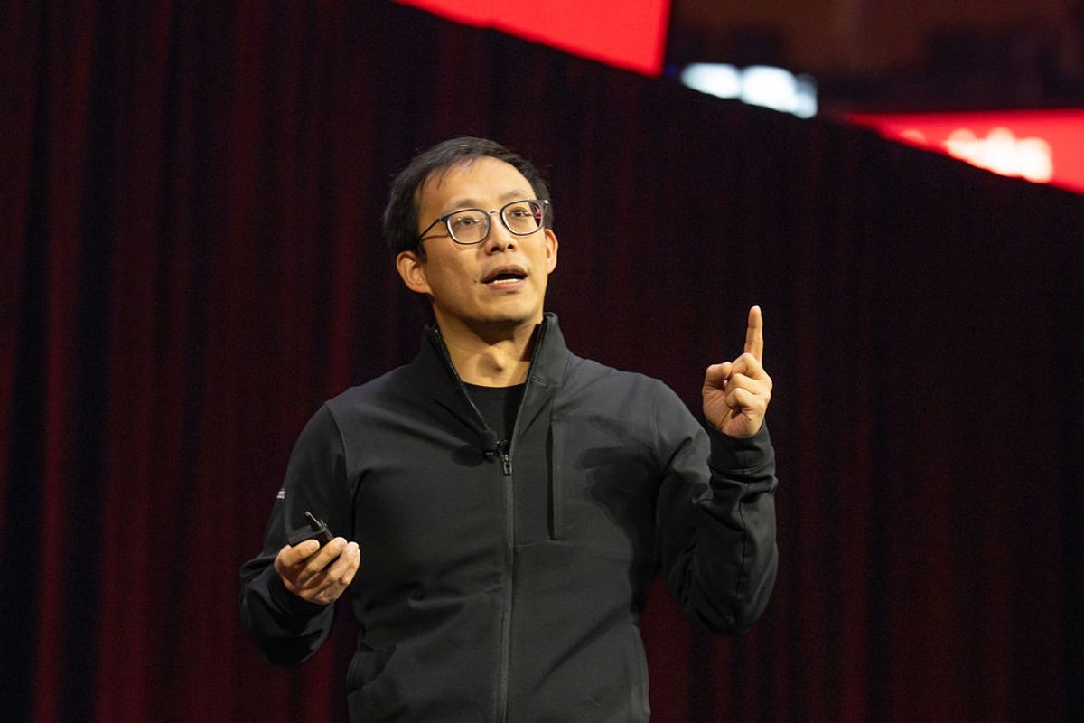 Speaker in black jacket gesturing with finger raised during presentation at conference venue
