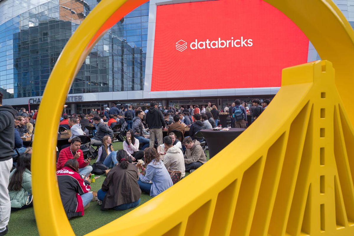 Attendees seated on green turf viewing large Databricks branded screen through yellow sculptural frame