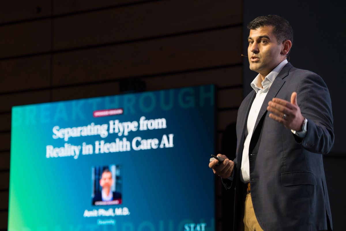 Speaker presenting at conference with slide about separating hype from reality in health care AI