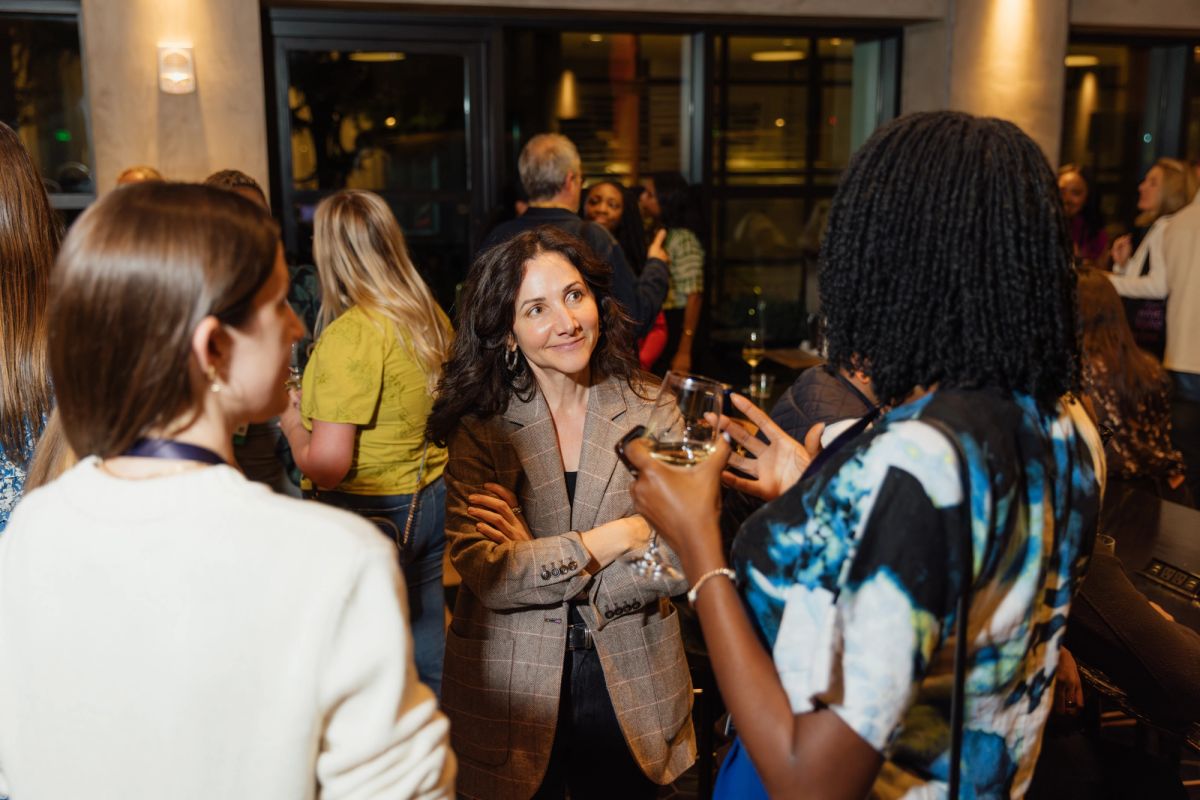 Conference attendees networking and conversing in a modern venue lobby with glass doors and warm lighting.