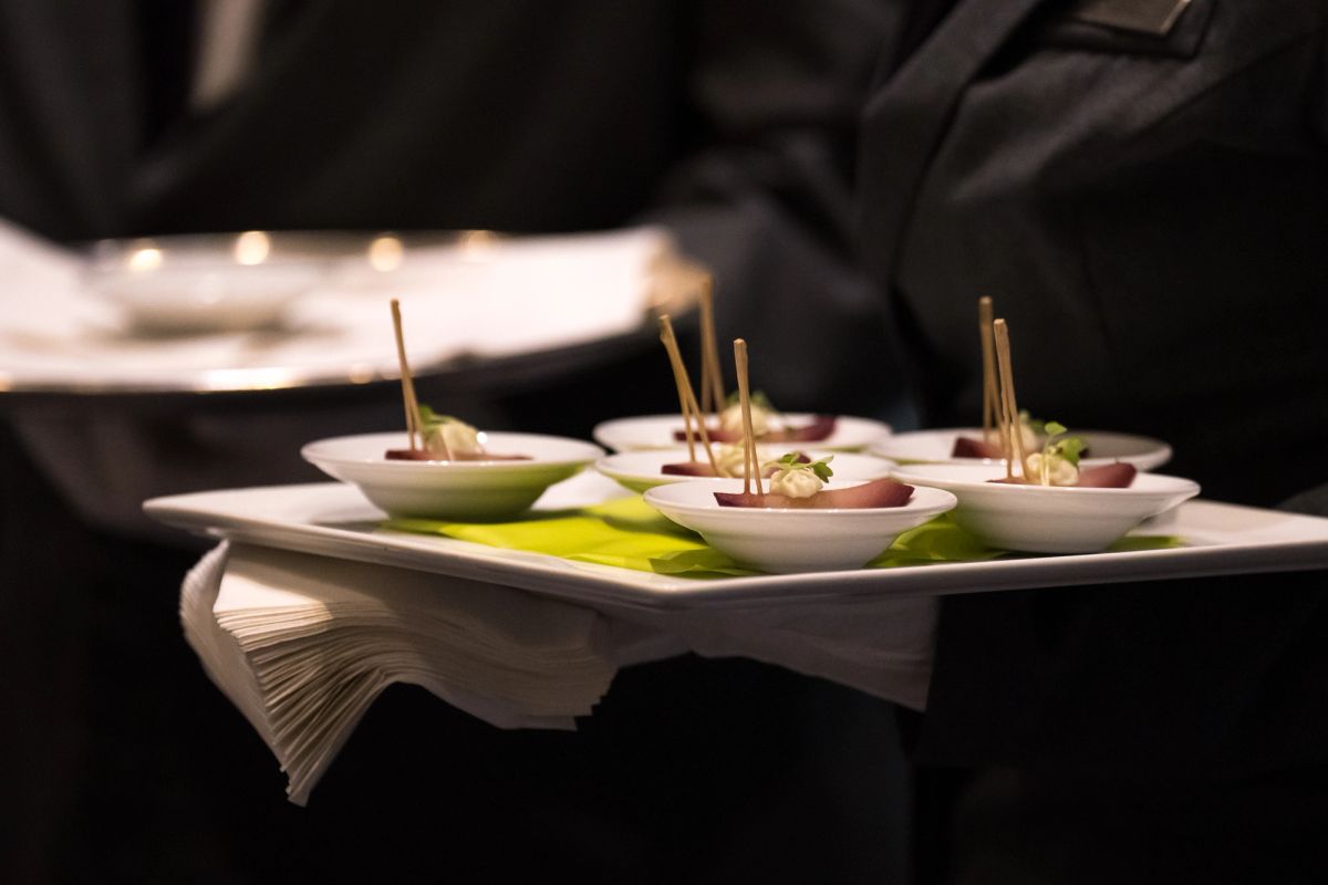 Server carrying elegant appetizer plates with small bowls and toothpicks at upscale event venue