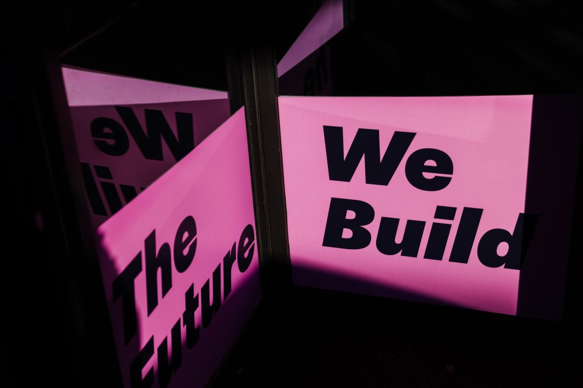 Pink illuminated signs reading "We Build" and "The Future" displayed at a conference venue