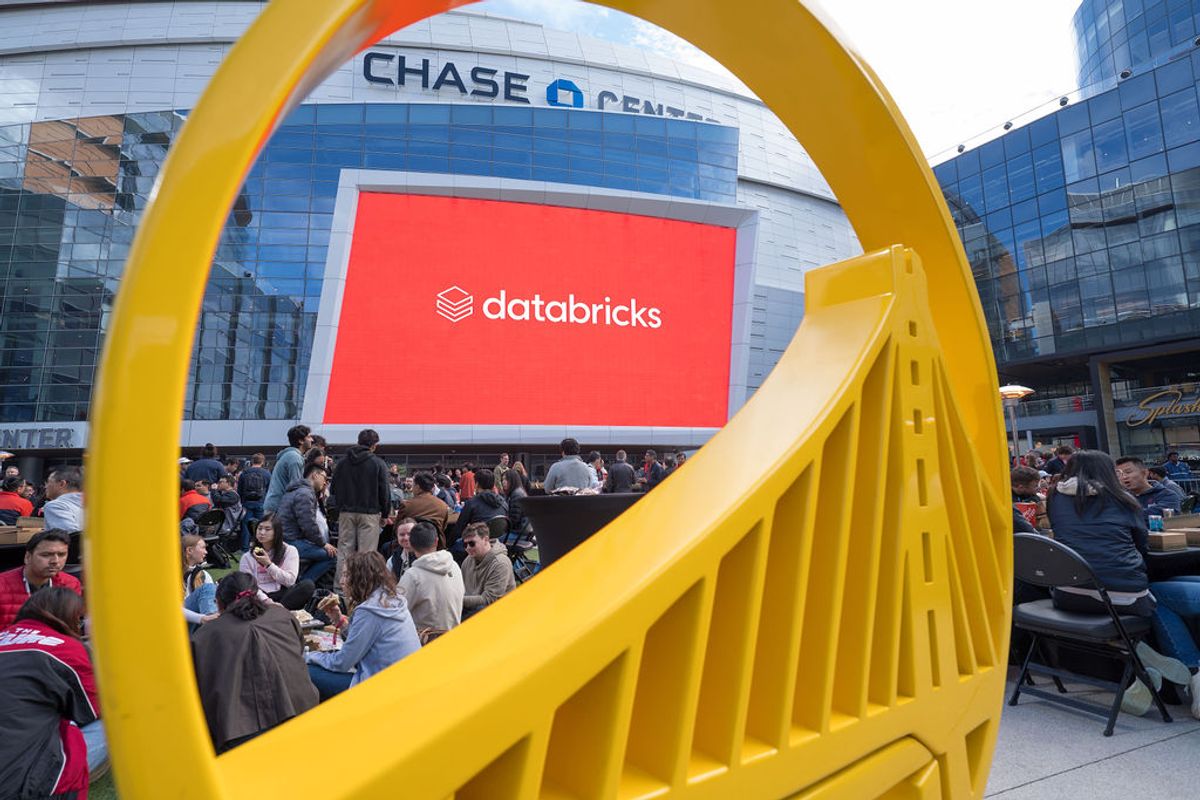 Conference attendees seated outdoors with large yellow sculptural element and Databricks logo on screen at.