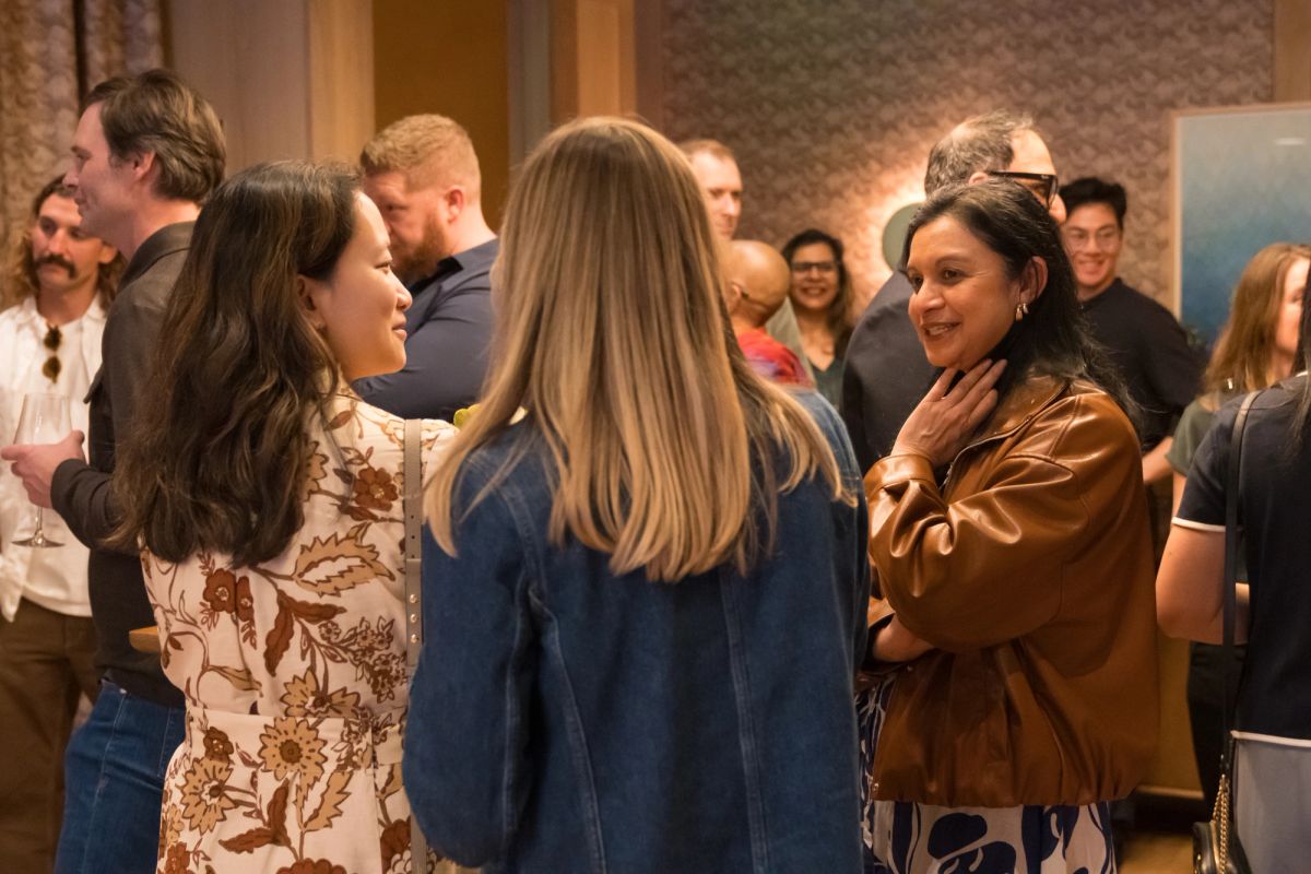 Attendees networking and conversing in small groups at an indoor event with warm lighting and brick walls.