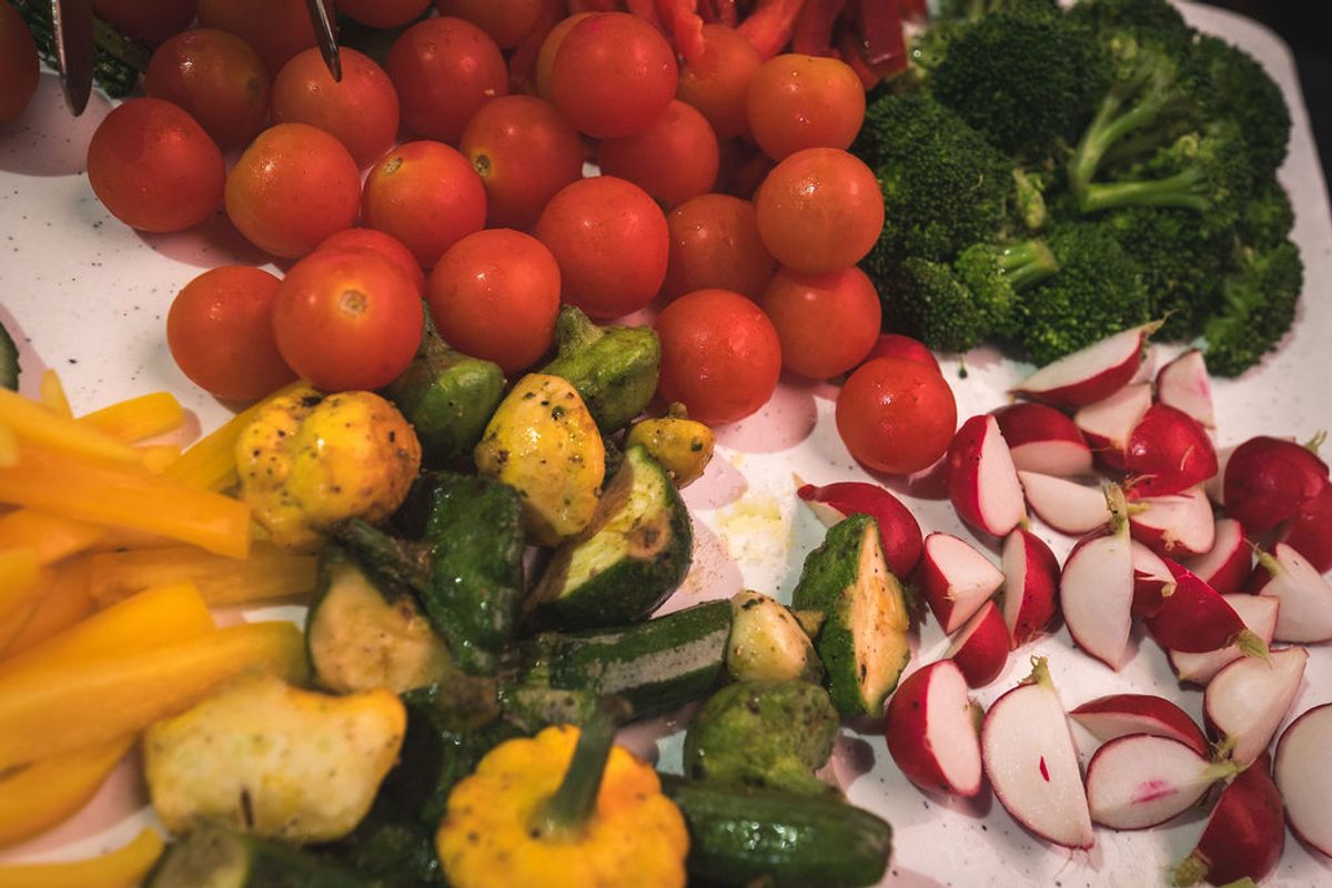 Fresh vegetables including cherry tomatoes, broccoli, sliced radishes, and seasoned potatoes arranged on.