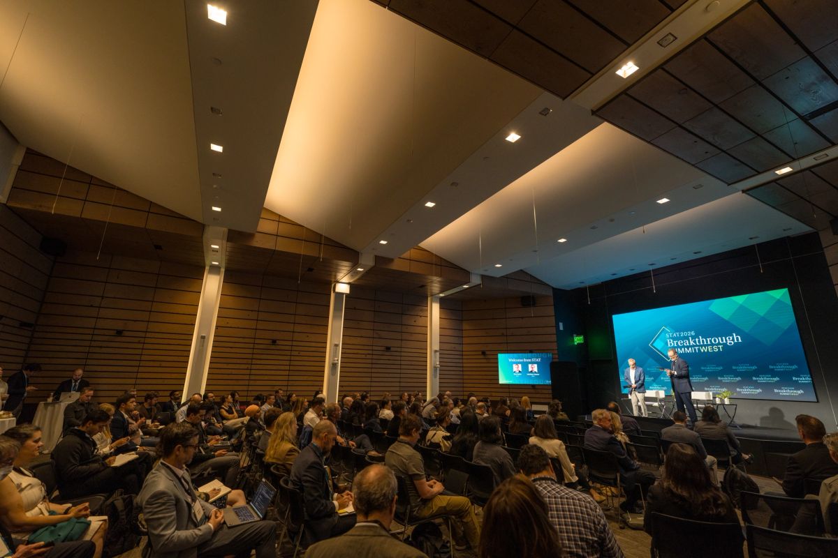 Speaker presenting to seated audience in modern auditorium with large screen displaying "Breakthrough" text