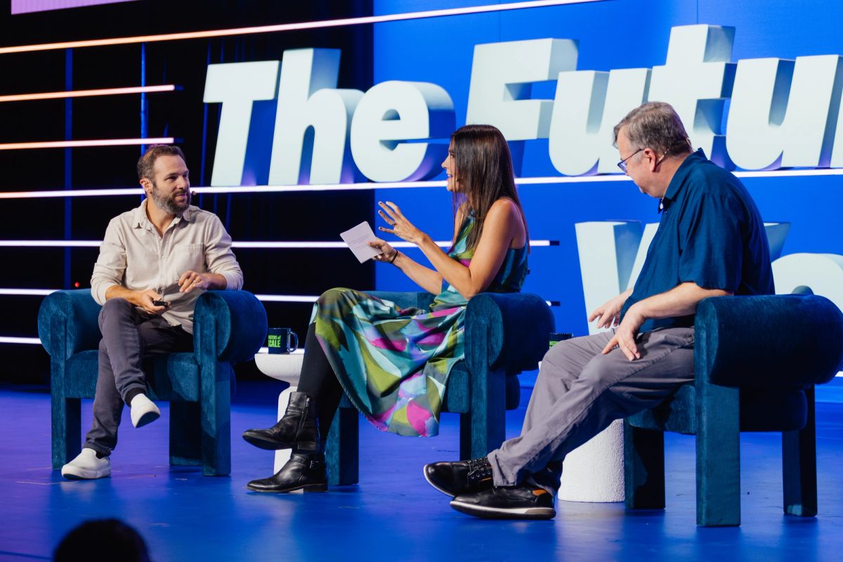 Three people in discussion on stage with blue backdrop displaying "The Futu" text at conference venue.