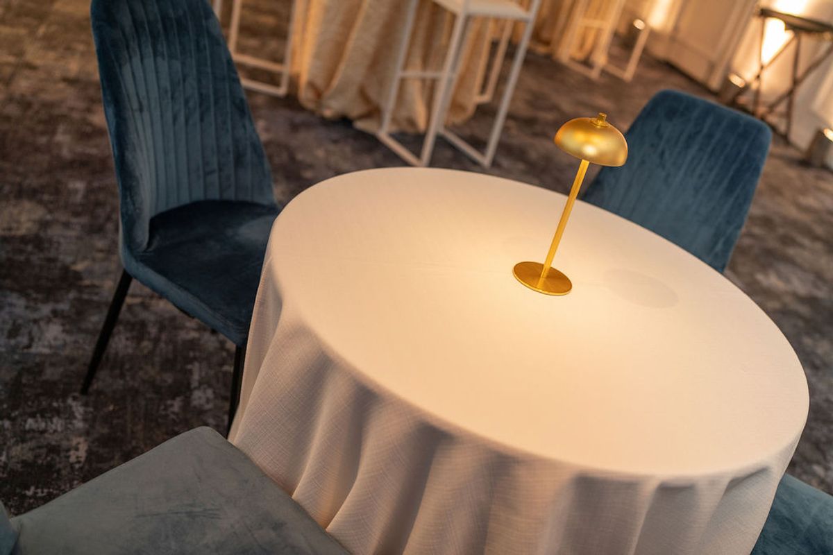 Round table with white tablecloth and gold lamp surrounded by blue upholstered chairs in elegant venue