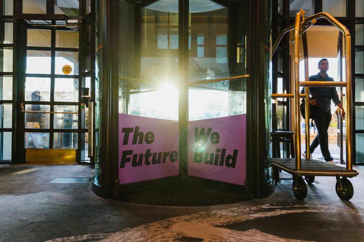 Hotel lobby with revolving door displaying "The Future We Build" text and luggage cart with attendee