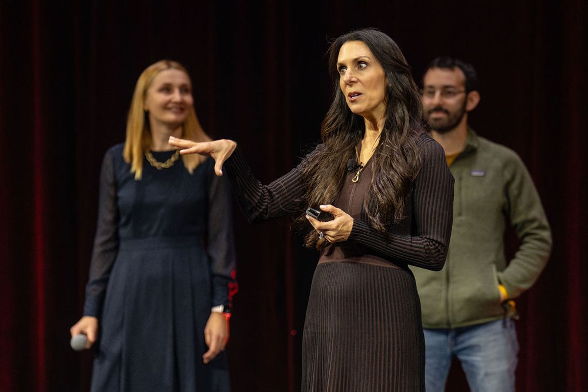 Speaker presenting on stage with two people in background at conference event