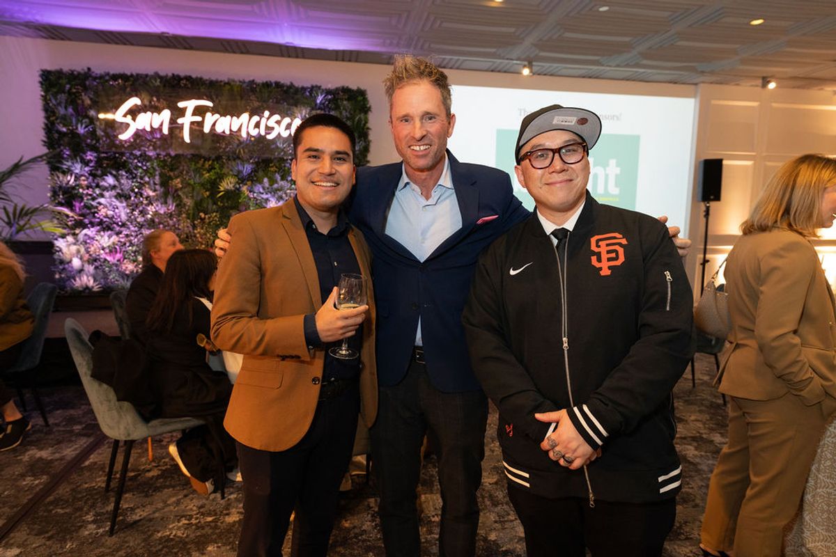 Three men pose together at a networking reception, with San Francisco signage visible in the background.