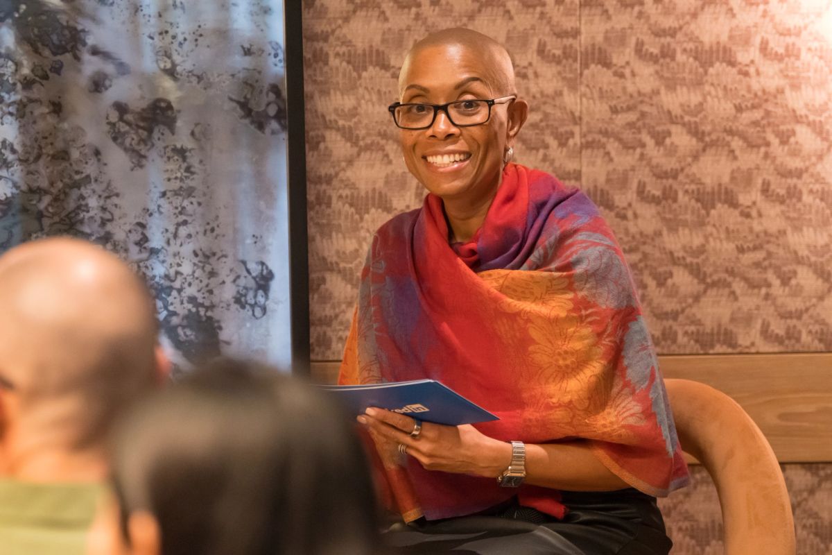 Speaker in colorful shawl smiles while holding papers during panel discussion, with attendee visible in.