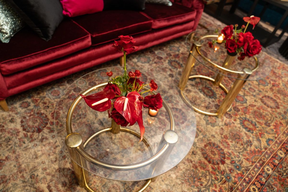 Two glass coffee tables with gold frames hold red floral arrangements on a patterned rug near a red sofa.