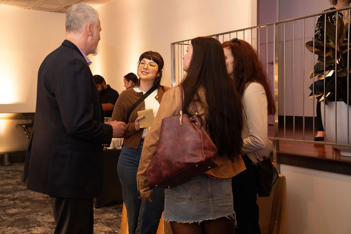 Business professional in suit speaks with two young women at networking reception in upscale venue