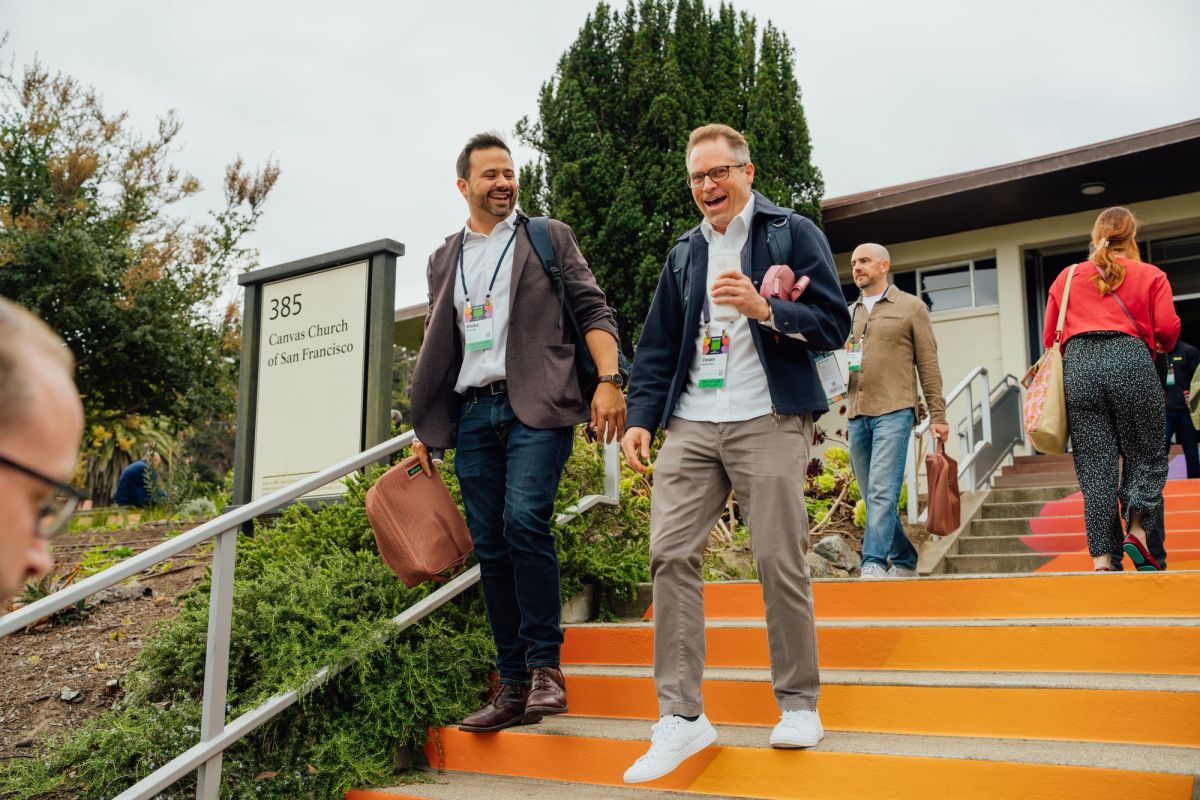 Two men with conference badges walk down orange steps while other attendees are visible in background