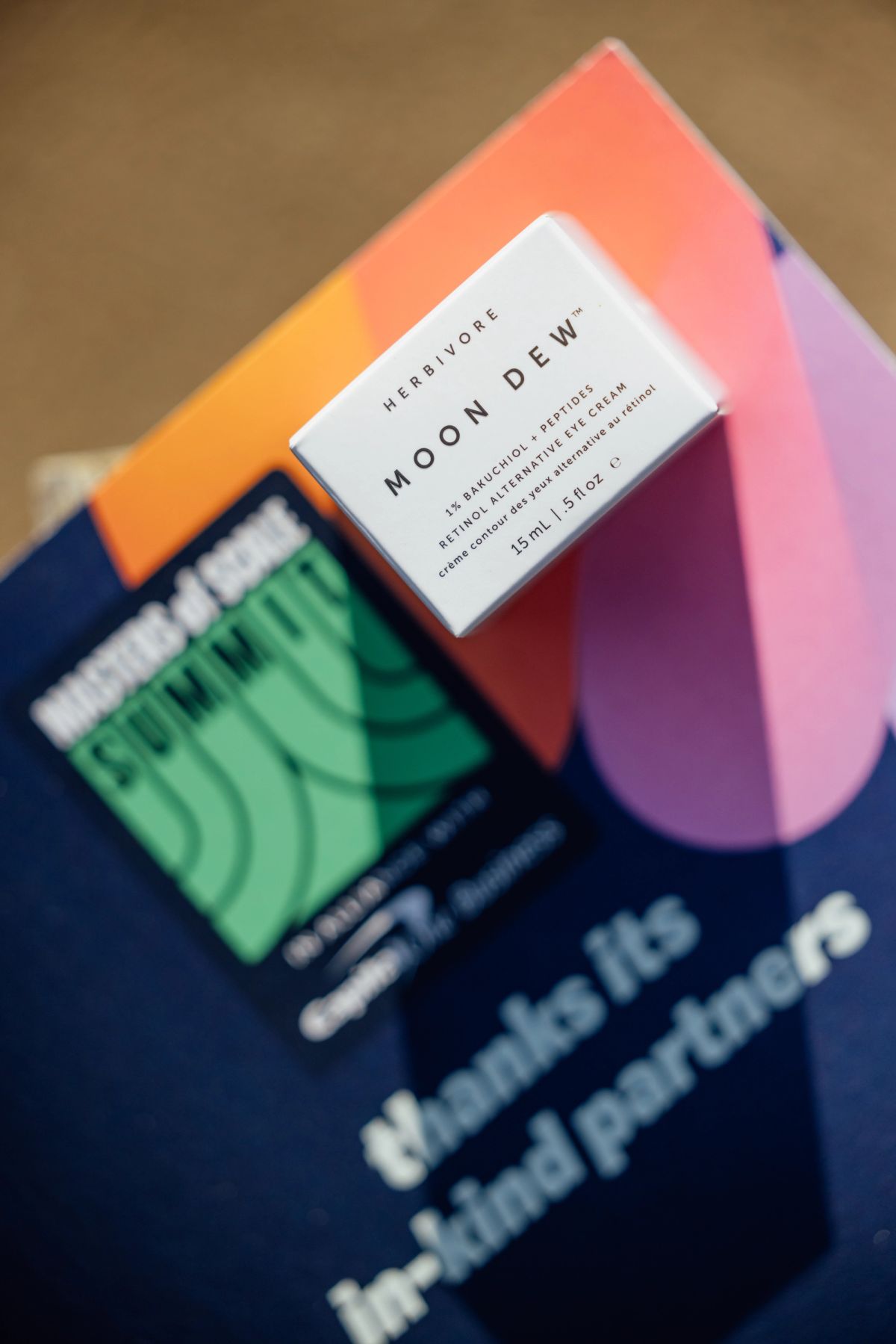 Herbivore Moon Dew skincare product on colorful geometric backdrop with blurred books below