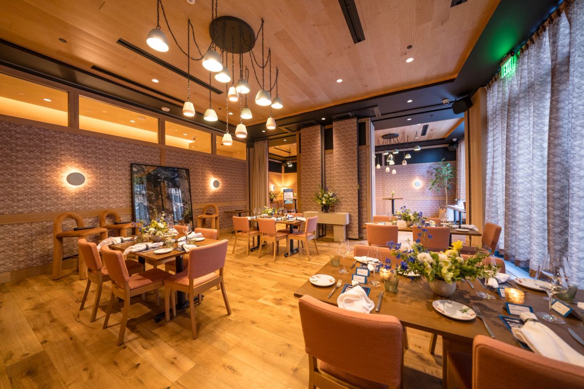 Modern restaurant dining room with wooden tables, upholstered chairs, pendant lighting, and brick walls
