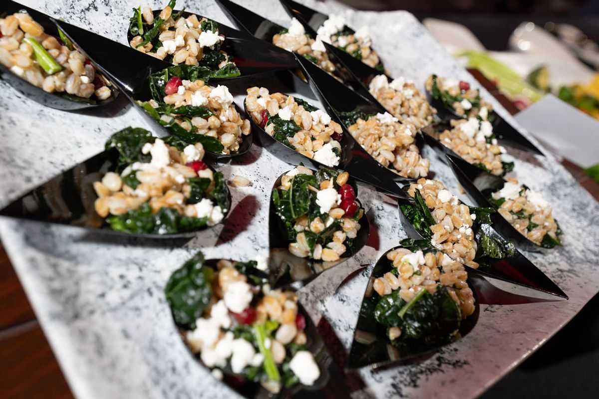 Black spoons filled with grain salad topped with greens, white cheese, and red garnish arranged on marble.