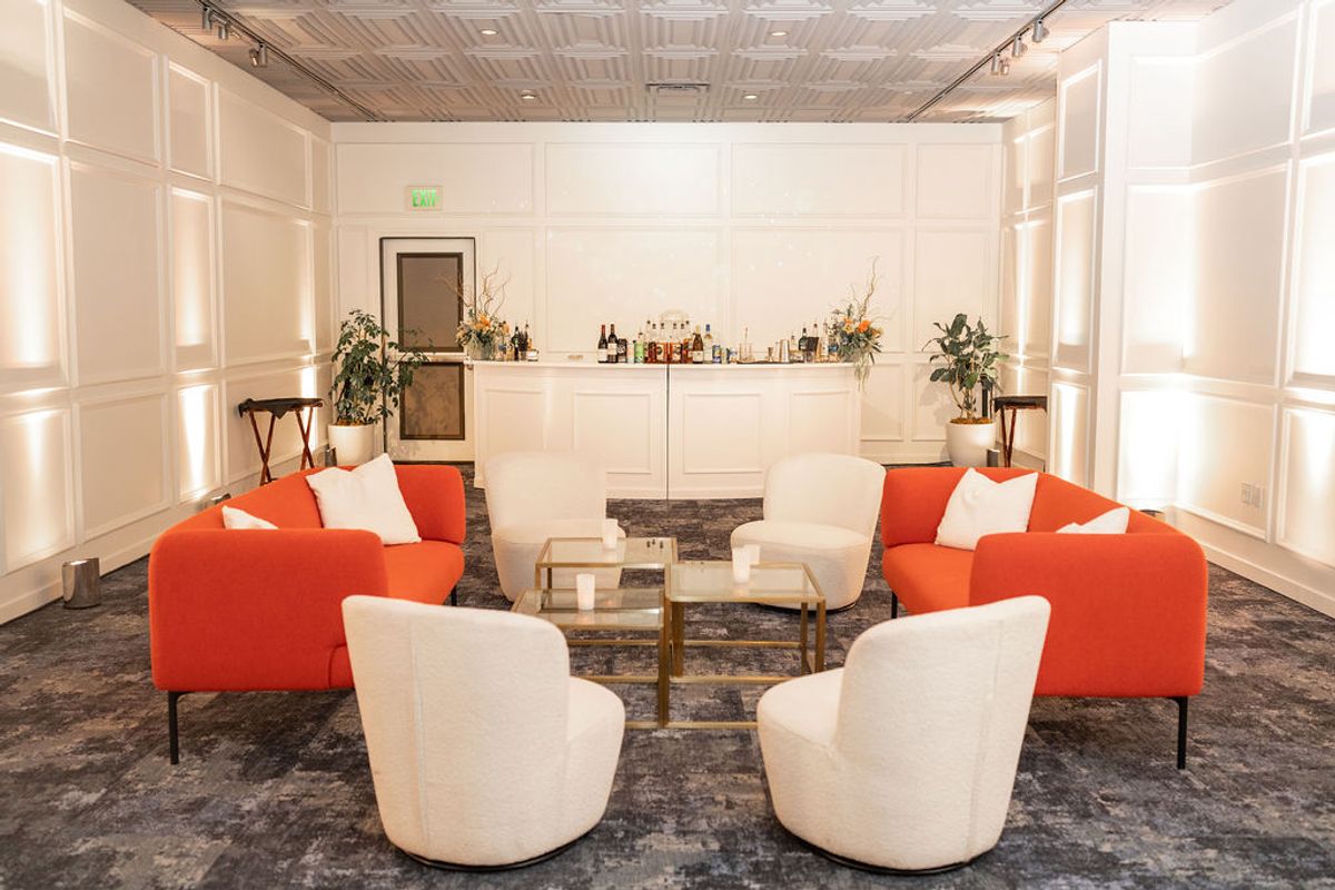 Modern lounge area with orange sofas, white chairs, and glass coffee table set up for networking reception