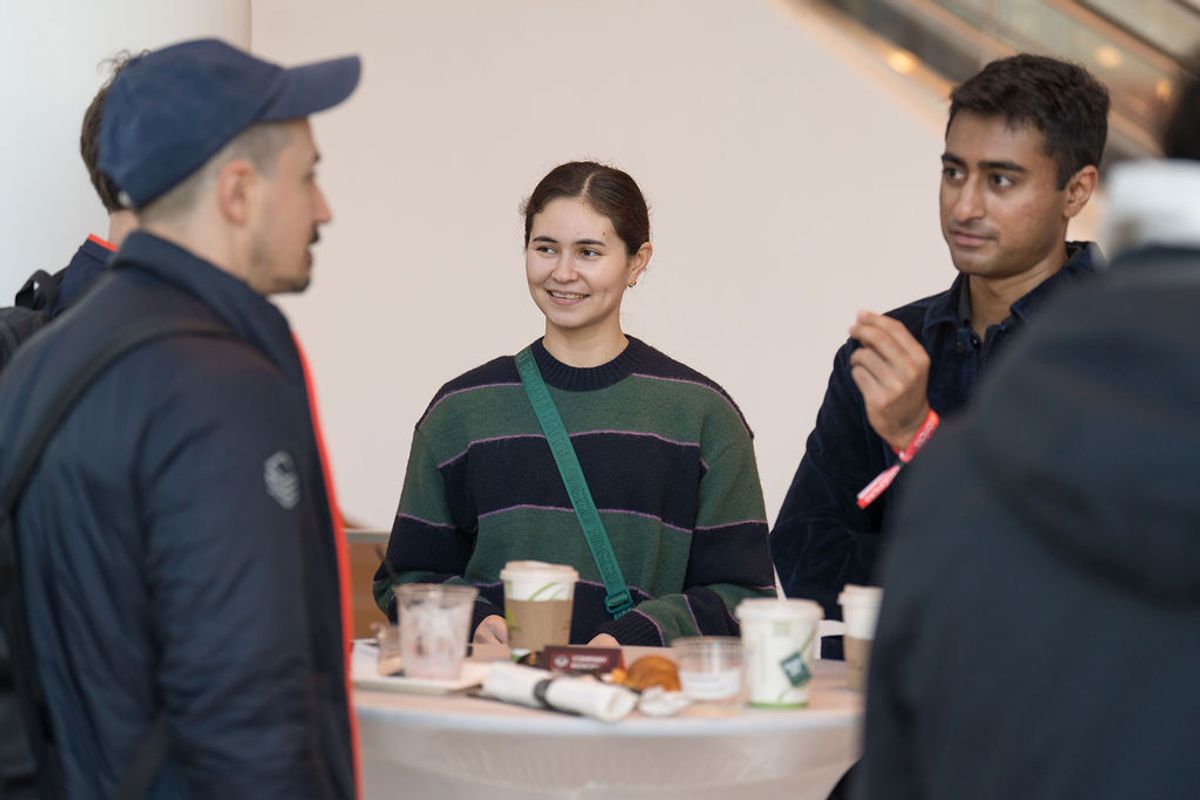 Three people networking at a conference table with drinks and food items in an indoor venue