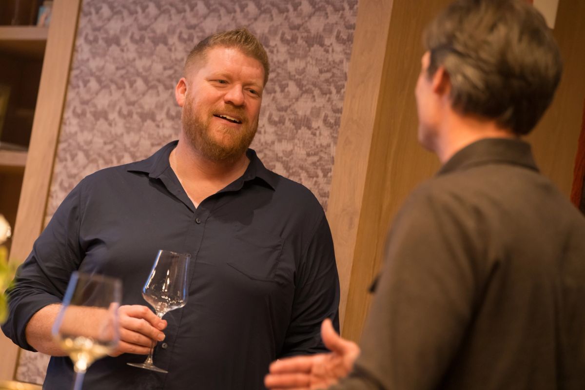 Two men networking with wine glasses at an indoor event, one in navy shirt smiling during conversation