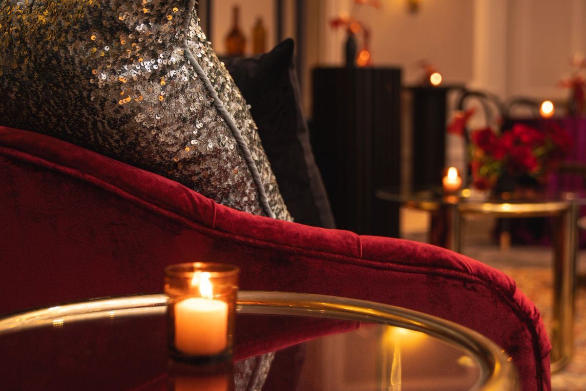 Elegant red velvet sofa with sequined pillows and lit candle on glass table in luxurious lounge setting