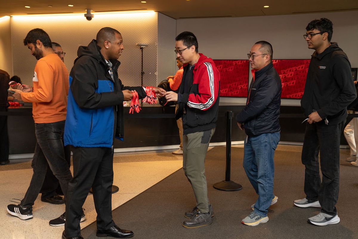 Conference attendees networking and exchanging materials in a modern venue lobby with red wall panels