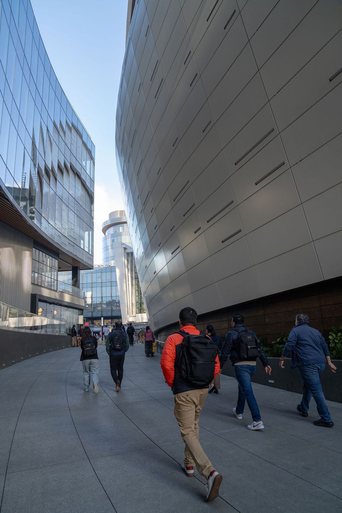 People walking through modern urban plaza between tall glass and metal buildings on clear day