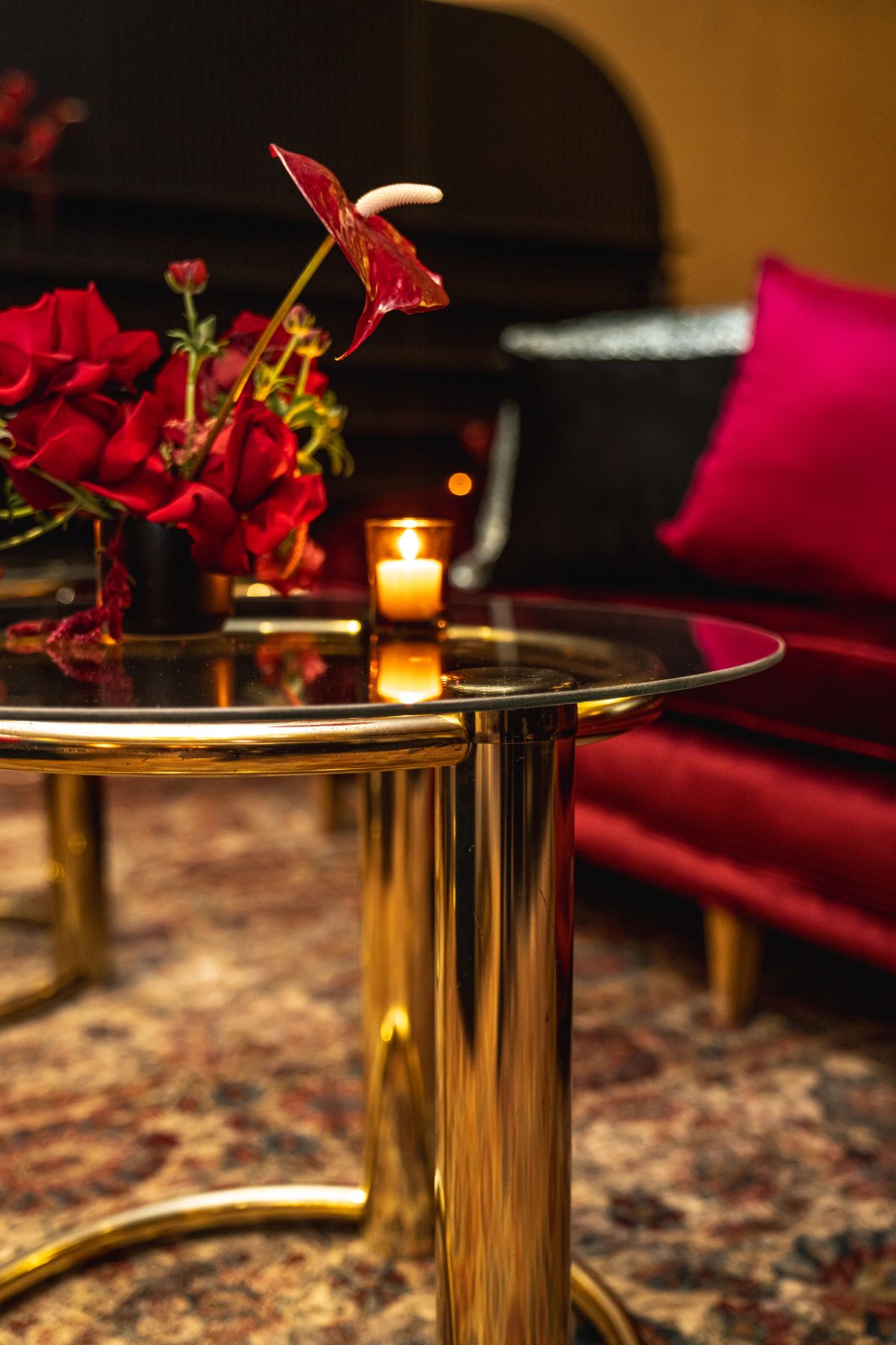 Glass coffee table with red flowers and candle in elegant hotel lounge with burgundy seating