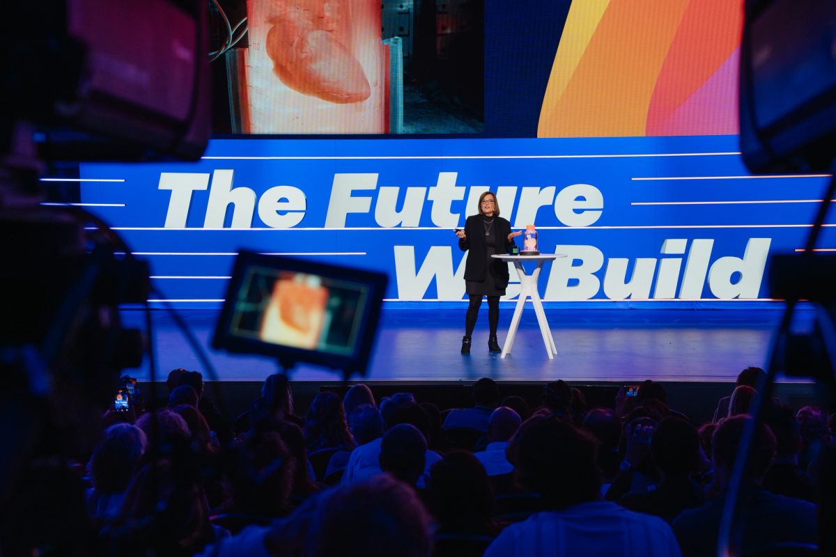 Speaker presenting on stage with "The Future We Build" backdrop to seated audience at conference venue
