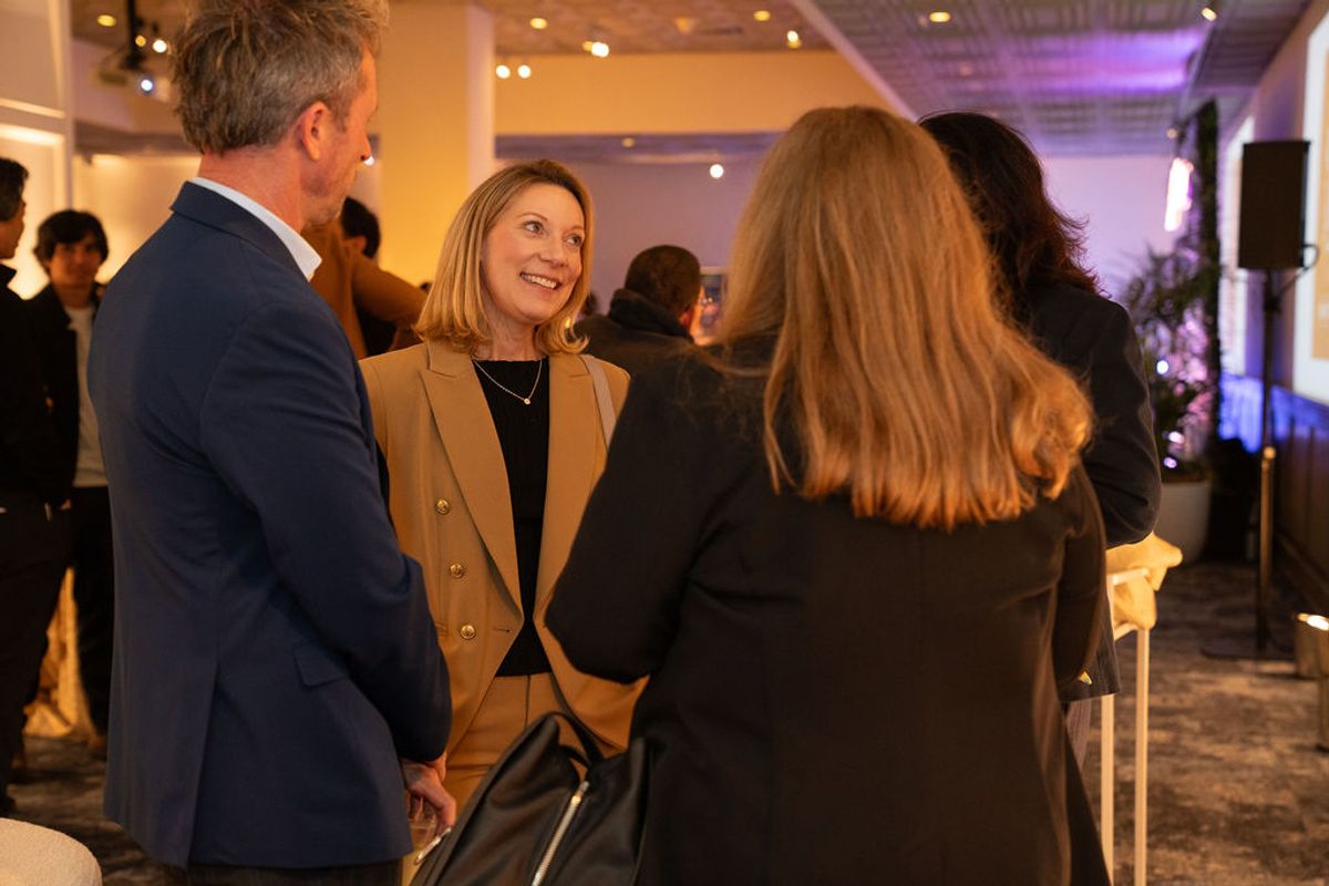 Business professionals networking and conversing at an upscale indoor reception venue with warm lighting.