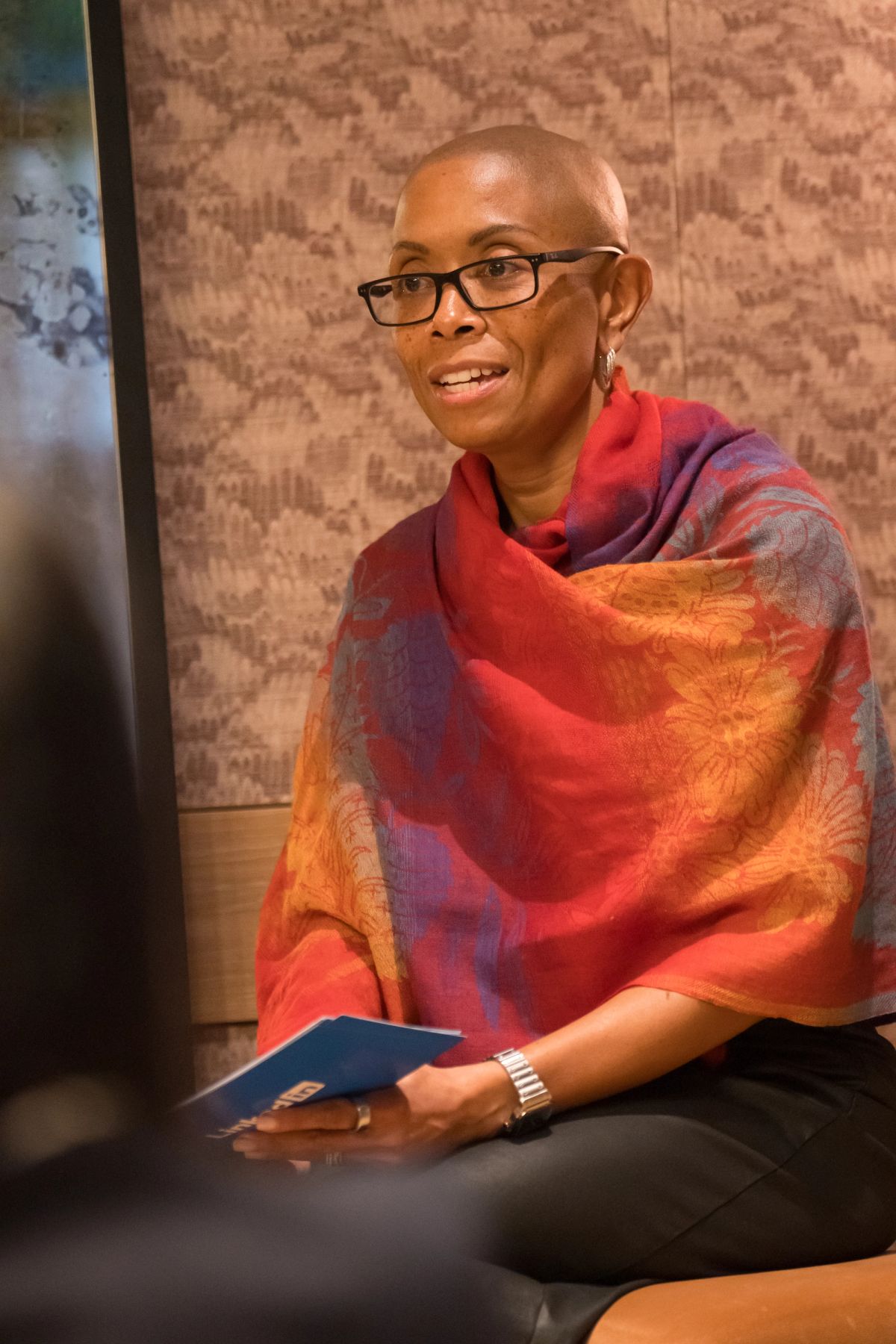 Speaker in colorful shawl and glasses sits at panel discussion table during event