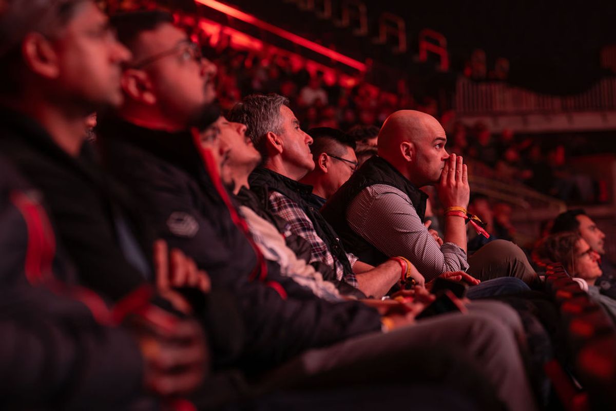 Attendees sitting in red-lit auditorium seats watching a conference presentation