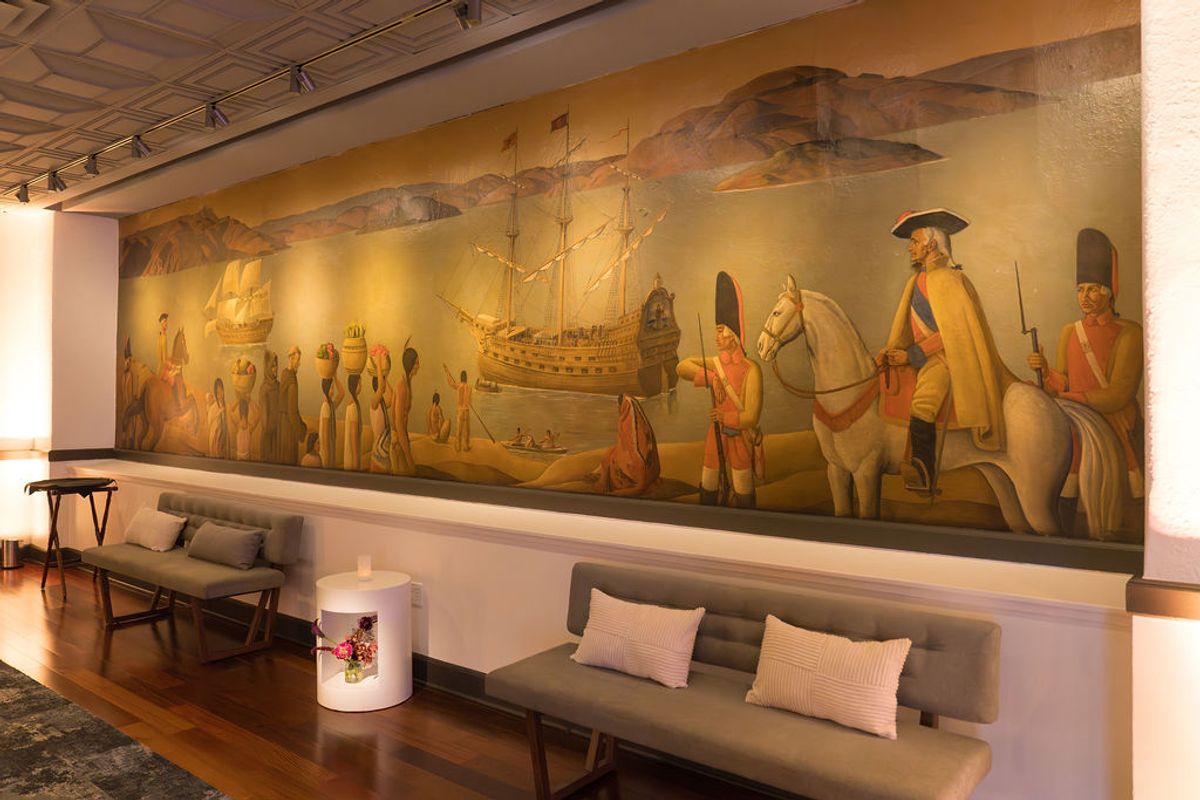 Modern seating area with historical mural depicting ships and colonial figures on wall above gray sofas