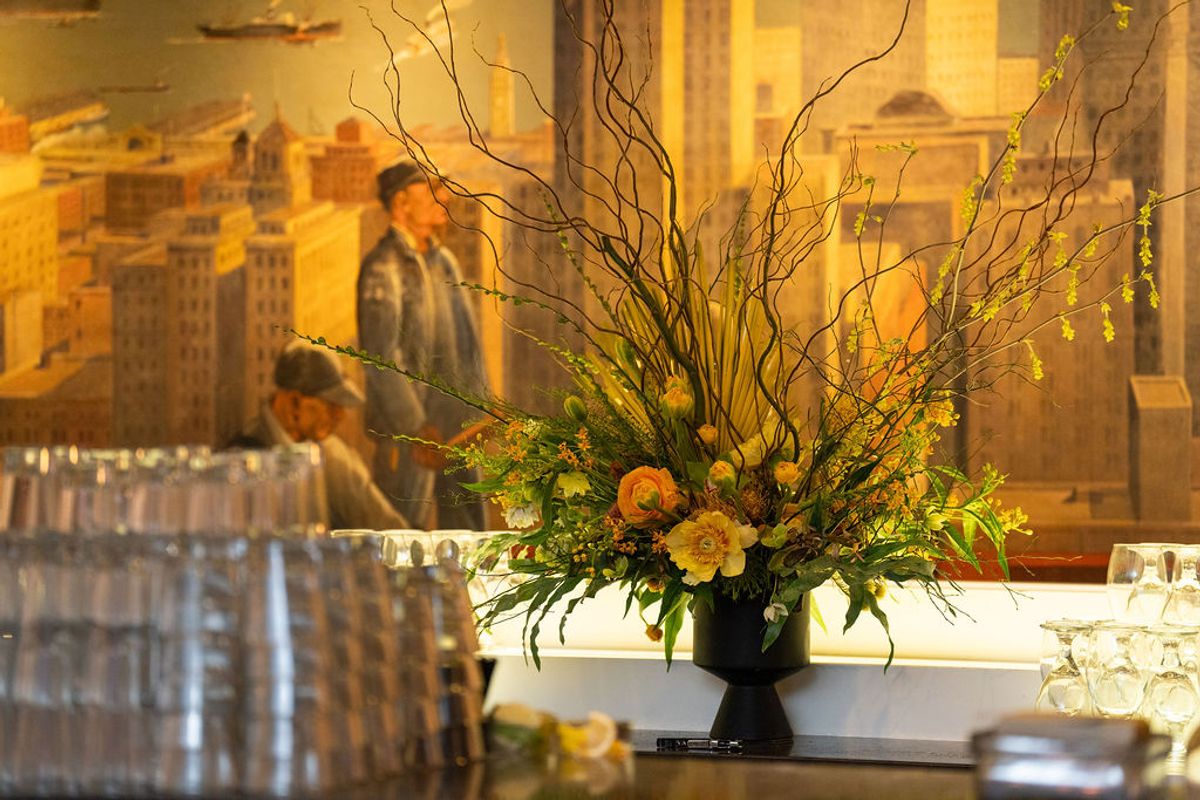 Large floral arrangement with branches and orange flowers on table at networking reception with attendees