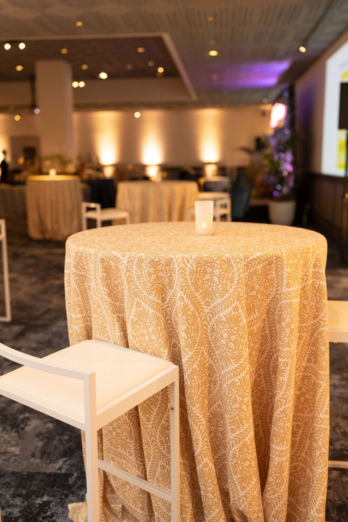 Round cocktail table with golden patterned tablecloth and wooden stool in upscale restaurant setting with.