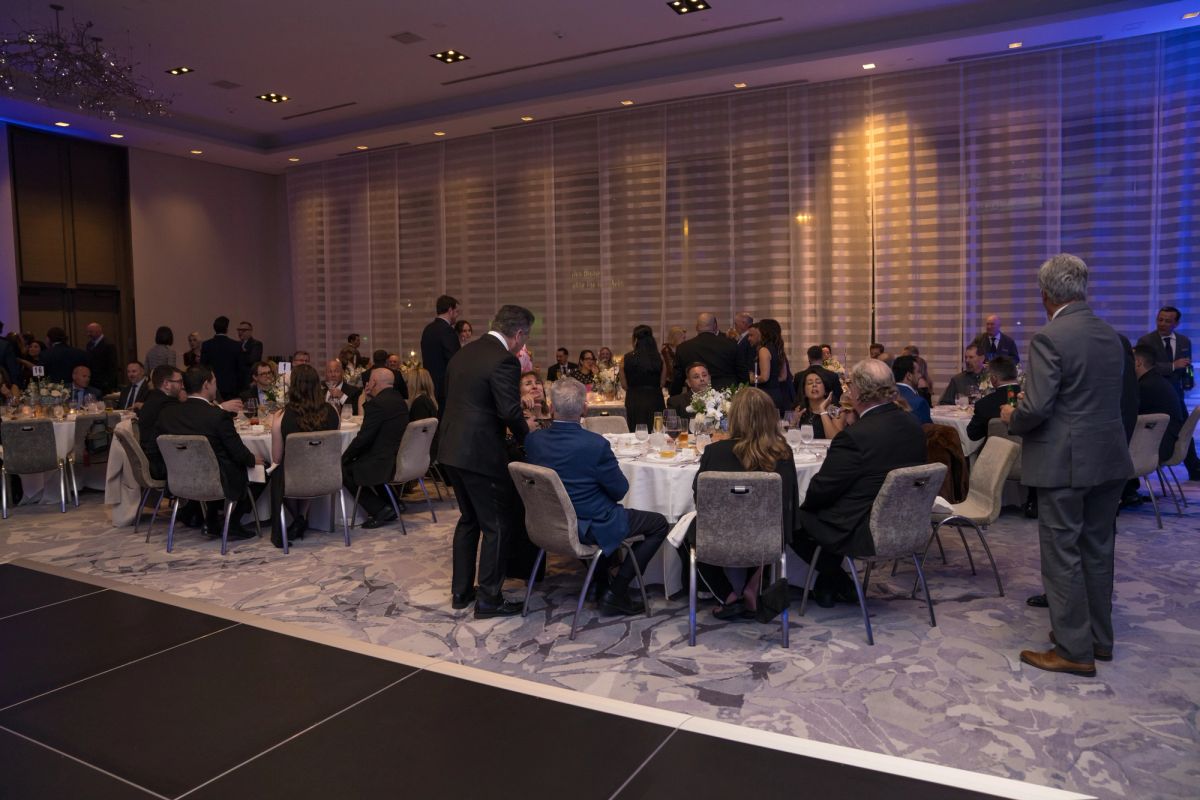 Formal dinner event with attendees seated at round tables in an elegant ballroom with blue lighting
