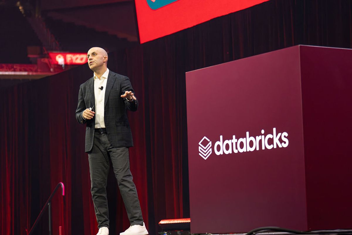 Speaker presenting on stage at Databricks conference with branded backdrop and red lighting