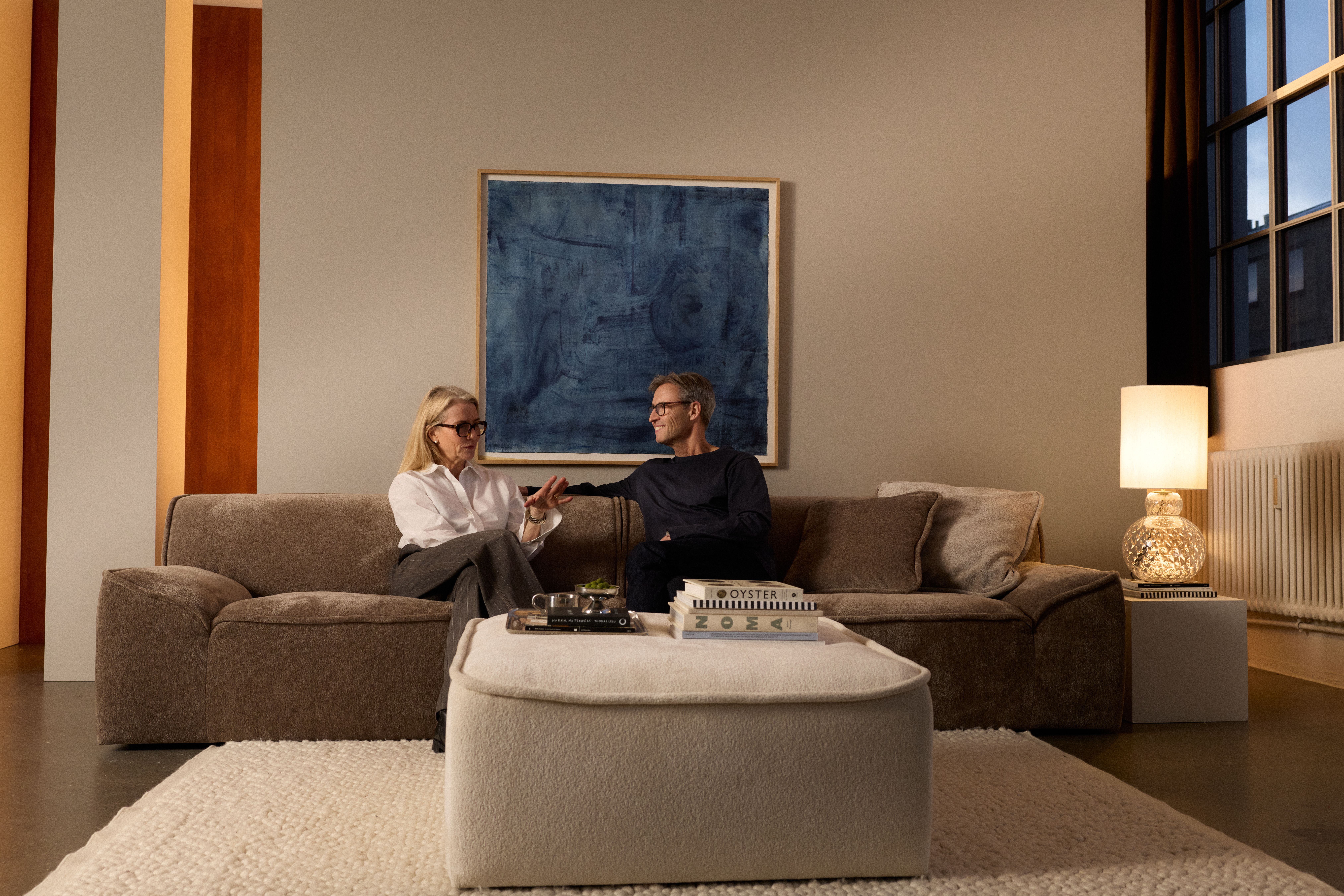 A man and a woman converse on a modern brown sofa in a stylish living room.